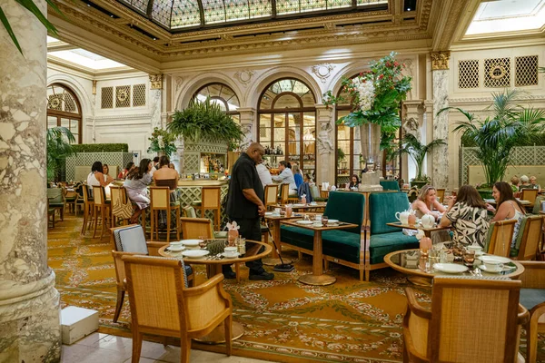 New York City, New York, ABD - 08.01.2024: New York 'ta sofistike bir otel salonu mermer sütunlar, kadife koltuklar ve boyalı cam bir tavan. Konuklar yeşillik ve klasik müzikle dolu müsrif bir atmosferde içki içip sohbet etmekten zevk alıyorlar.