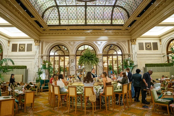 New York, New York, New York, ABD - 08.01.2024: Konuklar, New York 'ta lüks bir otel salonunda vitray tavan, mermer sütunlar ve yemyeşil yeşilliklerin yer aldığı merkez bir barda toplandılar. Varlıklı ortam klasik mimariyle gevşemiş mimariyi birleştirir.