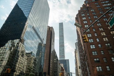 New York Citys Midtown 'ın çarpıcı manzarası. Gökdelenler ve trafik ışıkları bulutlu bir gökyüzüne karşı. Cam binalardaki yansımalar yakınlardaki klasik tuğla cepheleriyle tezat oluşturuyor..