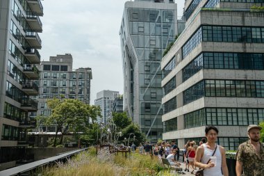 New York City, New York, ABD - 08.02.2024: Ziyaretçiler Manhattan 'daki çağdaş binalarla çevrili High Line parkı boyunca toplanıyorlar. Kentsel yeşillik ve ufuk çizgisi görüşleri modern şehir tasarımı ve turizmini vurguluyor.