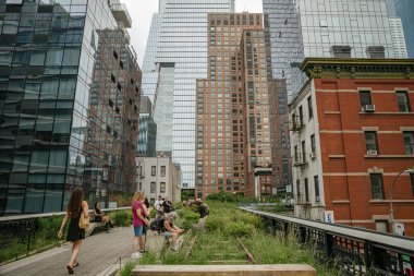 New York City, New York, ABD - 08.02.2024: İnsanlar Manhattan 'da cam gökdelenler ve arkalarında yükselen tuğla binalarla High Line parkı boyunca rahatlar ve yürürler. Sahne, New York 'ta çağdaş kentsel gelişim ve yeşil kamusal alan yakalıyor.