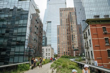 New York City, New York, ABD - 08.02.2024: İnsanlar Manhattan, New York 'ta modern cam gökdelenler ve tuğla binalarla çevrili High Line yüksek parkı boyunca yürüyor. Şehir mimarisi ve bereketli yeşillik canlı bir metropol yaratır.
