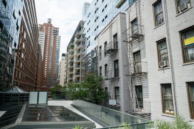 Eski metal yangın merdivenleri Manhattan 'daki modern cam dairelerin yanındaki beyaz bir bina. Tarihi ve çağdaş mimari arasındaki zıtlık, New York 'taki kentsel dönüşümü yansıtır..