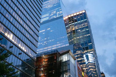 Modern cam gökdelenler Manhattan 'da mavi saatte parlıyor. Aydınlatılmış ofis pencereleri akşam gökyüzünü yansıtıyor. Sahne, New York 'taki kurumsal mimari ve finansal enerjiyi yakalıyor..
