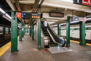New York metro istasyonunun içinde yürüyen merdiven, çıkış levhası ve West 4. Cadde Washington Meydanı 'ndaki Uptown tren istikametini gösteriyor. Yeşil çelik kolonları ve fayanslı duvarları olan şehir içi ulaşım merkezi..