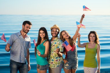 Guys and girls with American flags on the beach. clipart
