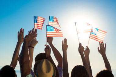 Gün batımında Amerikan bayrakları sallayarak gençler.
