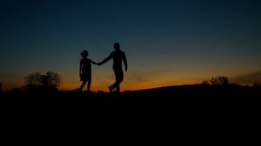 Tepelerde yürüyen erkek ve kızın silueti.