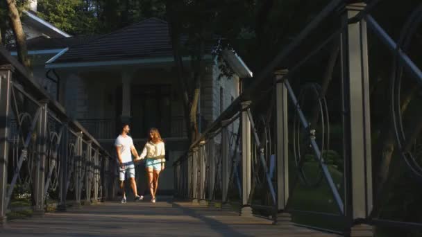 Lovers guy and girl walking on a bridge in the park. — Stock Video