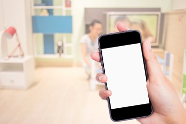 Arka plandaki yatak odasında cep telefonuyla fotoğraf çekiyor.