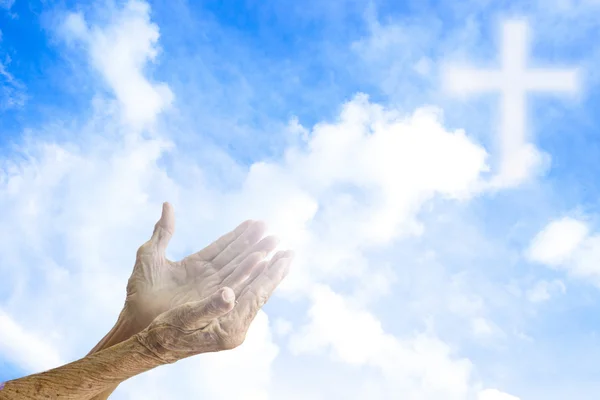 Hände älterer Frauen, die beten, verschwimmen das Kreuz am Himmel. — Stockfoto