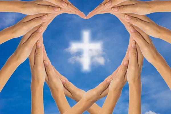 As mãos dão forma ao coração e a cruz cristã no céu . — Fotografia de Stock