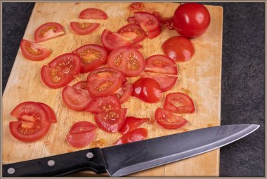 Ahşap kesim tahtasında dilimlenmiş domatesler pişirmeye hazırdır.