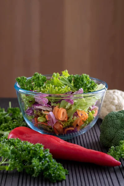 Fresh vegetables choped in the glass bowl with tomatos and parsley at foreground — Stock Photo, Image