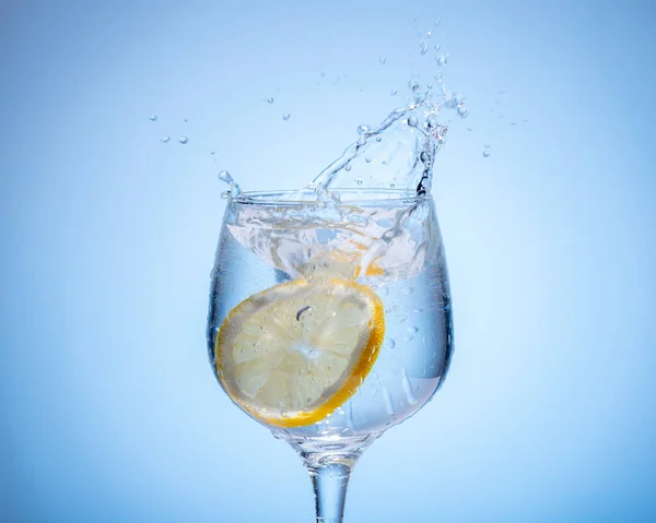 Glass of water with lemon droped in and splash — Stock Photo, Image