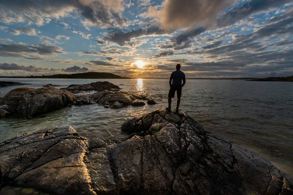 Silhouette of man standing on a rock and looking over sea toward the evening sun. — Stock Photo, Image