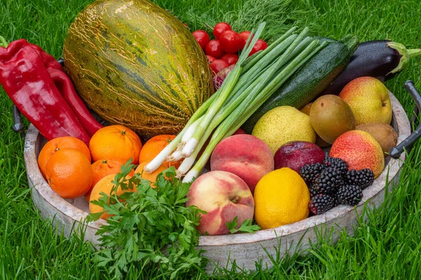 Obst und Gemüse in einer Holzschale auf grünem Gras als Hintergrund — Stockfoto