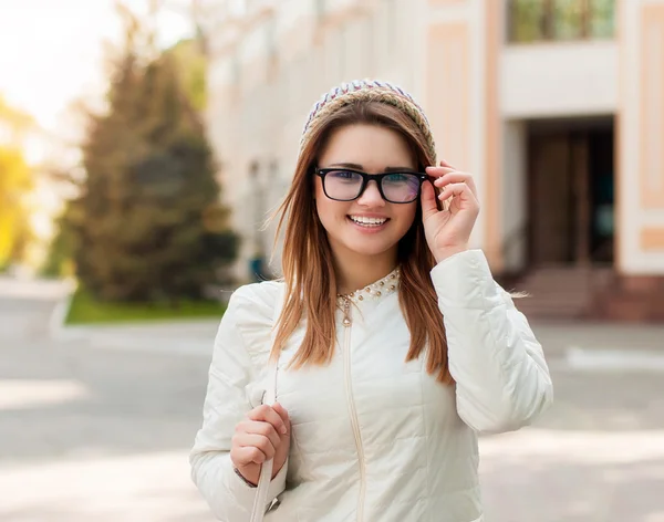 Una ragazza cammina per le strade. Ritratto di giovane donna sorridente in giacca bianca, occhiali e cappello. Bella donna all'aperto . — Foto Stock