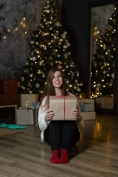 Noel ağacının yanında yerde oturan ve yılbaşı arifesinde hediyeler veren süveterli genç bir kadın. İçi Noel süslemeleriyle dolu..
