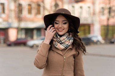 Baharda şehirde yürüyen kahverengi paltolu ve eşarplı güzel bir genç kız.