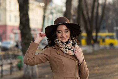 Baharda şehirde yürüyen kahverengi paltolu ve eşarplı güzel bir genç kız.