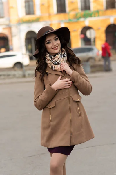 春には茶色のコートとスカーフで街を歩く美しい若い女の子 — ストック写真
