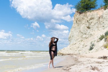 Siyah mayosu ve deniz kenarında poz veren güzel, şehvetli bir kız. Seksi vücutlu genç bir kadın yaz tatilinde dinleniyor. Mayo konsepti. Yaz yaşam tarzı