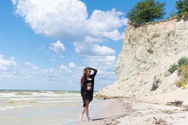 Siyah mayosu ve deniz kenarında poz veren güzel, şehvetli bir kız. Seksi vücutlu genç bir kadın yaz tatilinde dinleniyor. Mayo konsepti. Yaz yaşam tarzı