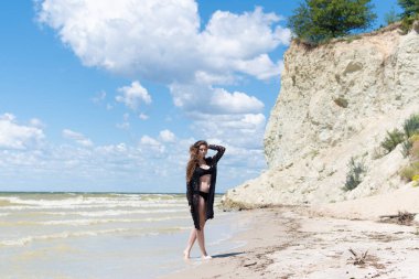 Siyah mayosu ve deniz kenarında poz veren güzel, şehvetli bir kız. Seksi vücutlu genç bir kadın yaz tatilinde dinleniyor. Mayo konsepti. Yaz yaşam tarzı