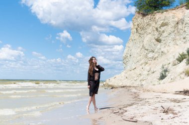 Siyah mayosu ve deniz kenarında poz veren güzel, şehvetli bir kız. Seksi vücutlu genç bir kadın yaz tatilinde dinleniyor. Mayo konsepti. Yaz yaşam tarzı