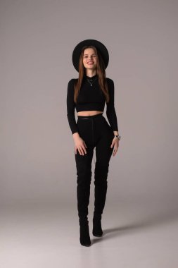 Siyah elbiseli ve şapkalı şık bir bayan stüdyoda poz veriyor.