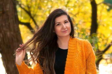 Sonbahar arka planında sarı kazaklı mutlu kız. Güzel çekici kız gülümsüyor. Güzel bir sonbahar portresi. Parkta gezen kız sonbaharda