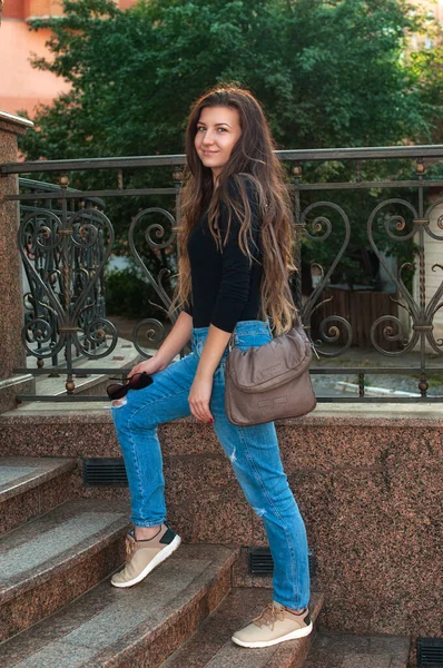 穿着手提包走在城市街道上的年轻时尚女人 穿着黑色衬衫和牛仔裤的时髦女模特 — 图库照片