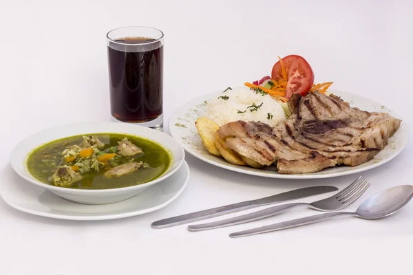 Peruvian Dish: Chicken soup of coriander (aguadito de pollo)+chicha morada (purple corn  juice) and barbecue grilled with rice, potatoes and salad — Stock Photo, Image