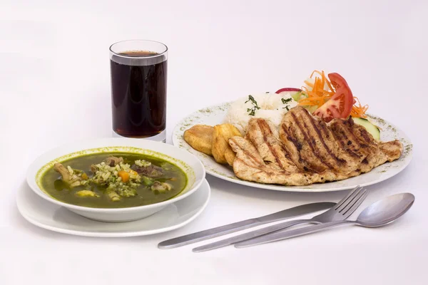 Peruviansk parabol: Kyllingesuppe af koriander (aguadito de pollo) + chicha morada (lilla majssaft) og kylling grillet med ris og salat . - Stock-foto