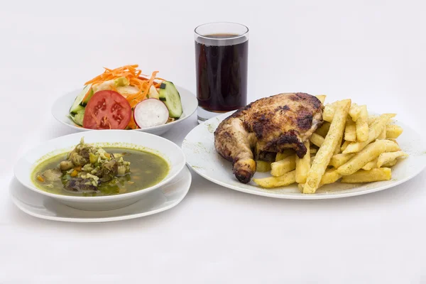 Gebratene Hähnchenkeule mit Pommes-Kartoffeln, "pollo a la brasa" genannt. Menü mit frischem Salat, Hühnersuppe aus Koriander (aguadito de pollo) + Chicha morada (lila Maissaft)) — Stockfoto