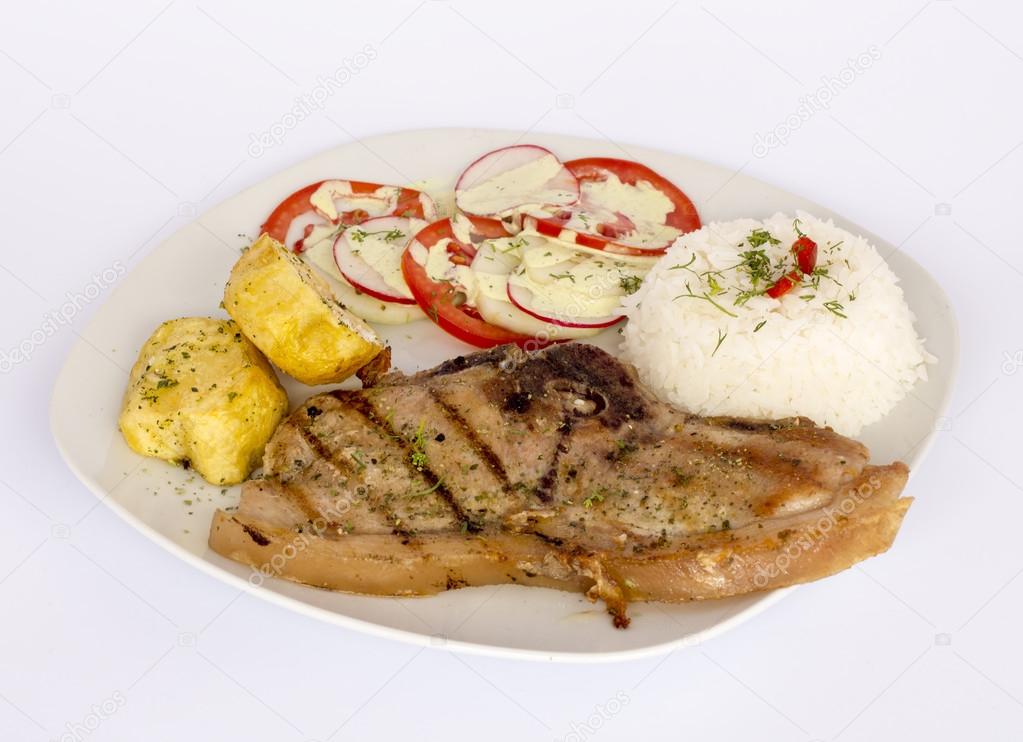 Grilled steak pork meat with salad, rice, potatoes, tomatoes served with a glass