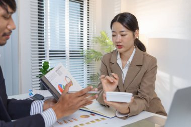 İki iş adamı modern bir ofiste finansal çizelge ve stratejileri tartışıyor. Resmi bir toplantıda fikir alışverişinde bulunur, raporları analiz eder ve çözümleri müzakere ederler..