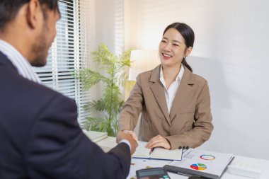 İş ortakları toplantılarını bir tokalaşma ile sonuçlandırır, güven, anlaşma ve başarılı işbirliğini sembolize eder. Çizelge ve raporları inceledikten sonra kararları doğrularlar..