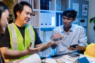Mimarlar ve mühendisler planlarını gözden geçirmek, fikir alışverişinde bulunmak ve şehir ortamında çağdaş bir inşaat projesi için planlarını geliştirmek için bir ofiste birlikte çalışırlar..