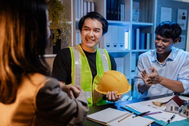 Mimarlar ve mühendisler planlarını gözden geçirmek, fikir alışverişinde bulunmak ve şehir ortamında çağdaş bir inşaat projesi için planlarını geliştirmek için bir ofiste birlikte çalışırlar..