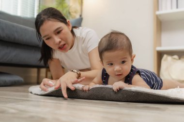 Anne sıcak bir gülümsemeyle onu cesaretlendirirken, bir bebek yumuşak bir paspasın üzerinde midede vakit geçirmekten zevk alır. Bu hassas an, erken gelişimi, aile bakımını ve evde kaynaşmayı vurguluyor.