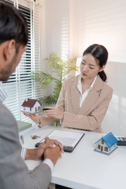 İki iş adamı emlak yatırımını tartışıyor, emlak sözleşmeleri imzalıyor ve ev modellerini gözden geçiriyor, konut satışlarını, finansmanı ve başarılı anlaşmaları sembolize ediyor.