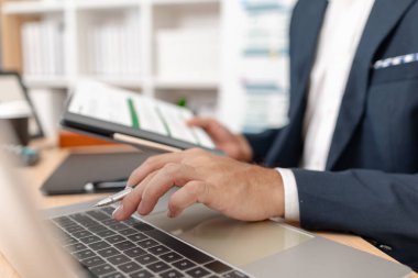 Takım elbiseli bir işadamı, şirket büyümesi ve uzun vadeli başarı için strateji, veri ve bütçe planlamasına odaklanan, parlak ve modern bir ofiste mali tabloları ve performans raporlarını analiz ediyor..