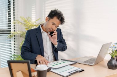 Temiz ve modern bir ofiste rapor ve çizelgeler kullanarak finansal hedeflere, yatırımlara ve stratejik başarılara odaklanarak bütçe hesaplayan ve şirket performansını gözden geçiren güvenilir bir işadamı.