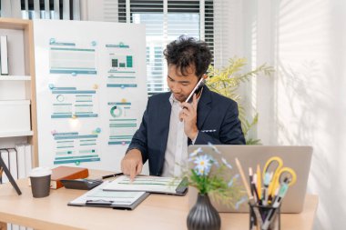 Temiz ve modern bir ofiste rapor ve çizelgeler kullanarak finansal hedeflere, yatırımlara ve stratejik başarılara odaklanarak bütçe hesaplayan ve şirket performansını gözden geçiren güvenilir bir işadamı.