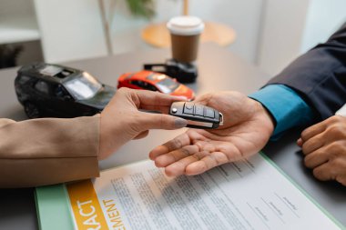 Bir işadamı ve müşteri, küçük model arabalar, bir kahve fincanı ve etraflarında araç satın alma pazarlığını sembolize eden belgeler içeren bir araba satış sözleşmesini inceliyor ve imzalıyor..