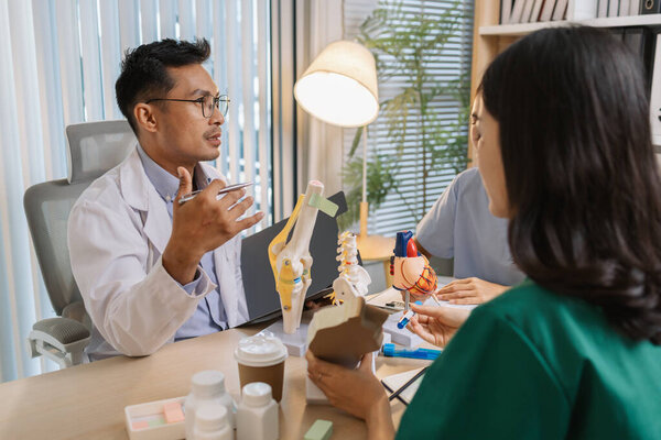 Врач преподает медицинскую команду во время клинического сеанса. Специалисты здравоохранения учатся вместе, обсуждая анатомические модели и случаи пациентов для повышения медицинских знаний и навыков лечения.