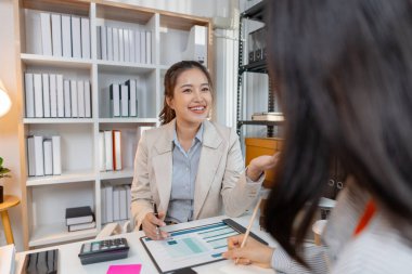 İki Asyalı iş kadını modern bir ofiste fikirleri tartışıyor ve belgelerden gelen raporları analiz ediyor. Başarı için iş stratejileri, takım çalışması ve organizasyon planlamasında işbirliği yaparlar..