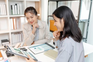 İki Asyalı iş kadını şirket stratejisini modern bir ofiste tartışıyor, finansal belge ve çizelgeleri analiz ediyorlar. Gelecekteki iş geliştirme konusunda işbirliği yapıyorlar ve fikirlerini paylaşıyorlar..